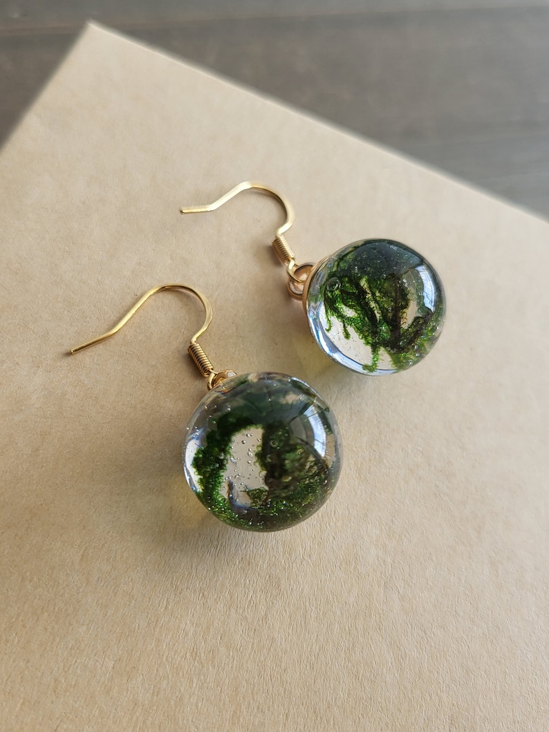 May include: A pair of gold dangle earrings with clear glass spheres containing preserved green moss.