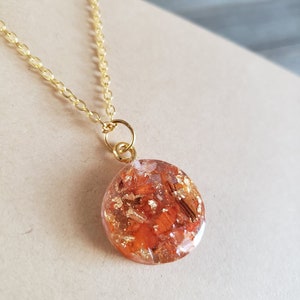 May include: A gold chain necklace with a round pendant featuring a resin design with orange and gold flakes.