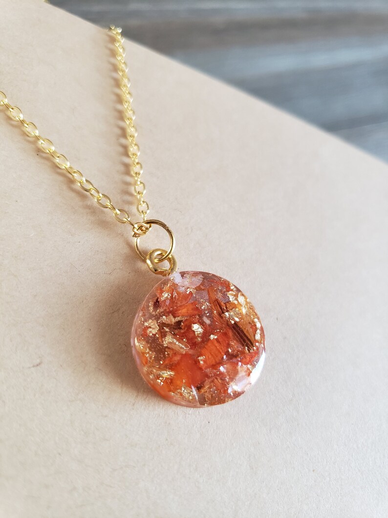 May include: A gold chain necklace with a round pendant featuring a resin design with orange and gold flakes.
