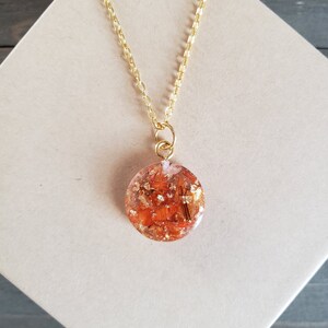 May include: A gold chain necklace with a round pendant featuring orange and gold flakes encased in clear resin.