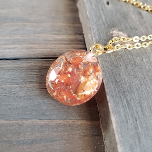May include: A gold chain necklace with a round pendant made of clear resin with red and gold flakes inside.