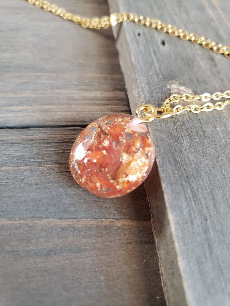 May include: A gold chain necklace with a round pendant made of clear resin with red and gold flakes inside.