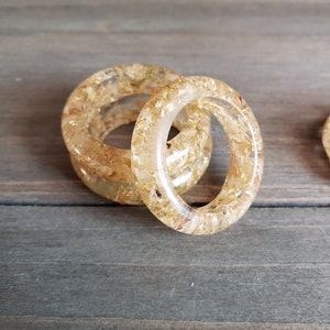 Op de afbeelding: Twee gouden harsringen met ingebedde gouden vlokken. De ringen zijn op elkaar gestapeld.