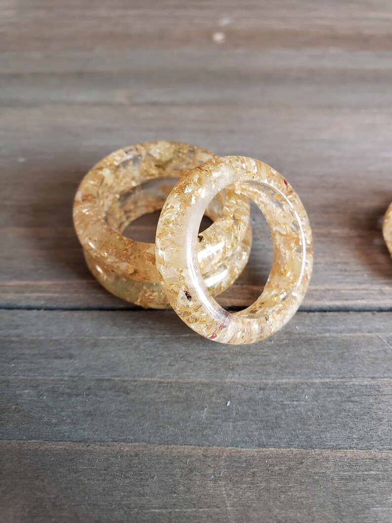 Op de afbeelding: Twee gouden harsringen met ingebedde gouden vlokken. De ringen zijn op elkaar gestapeld.