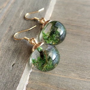 May include: Gold earrings with a green glitter ball charm. The ball is filled with green glitter and has a clear resin finish.