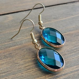 May include: A pair of gold dangle earrings with teal blue oval-shaped crystal stones.