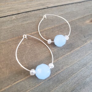 Puede incluir: Un par de pendientes de aro de plata con una piedra preciosa azul claro y detalles de cristal transparente.
