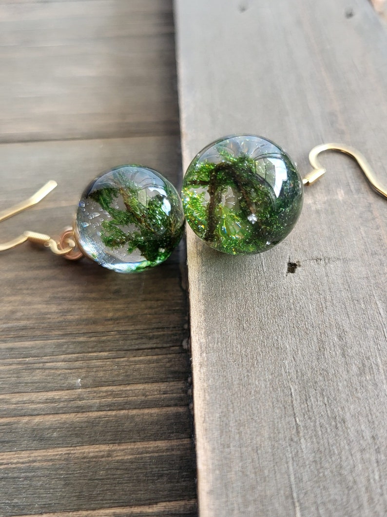 May include: A pair of gold dangle earrings with clear glass orbs containing preserved green moss.