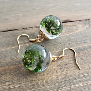 May include: A pair of gold earrings with clear glass spheres containing preserved green moss.