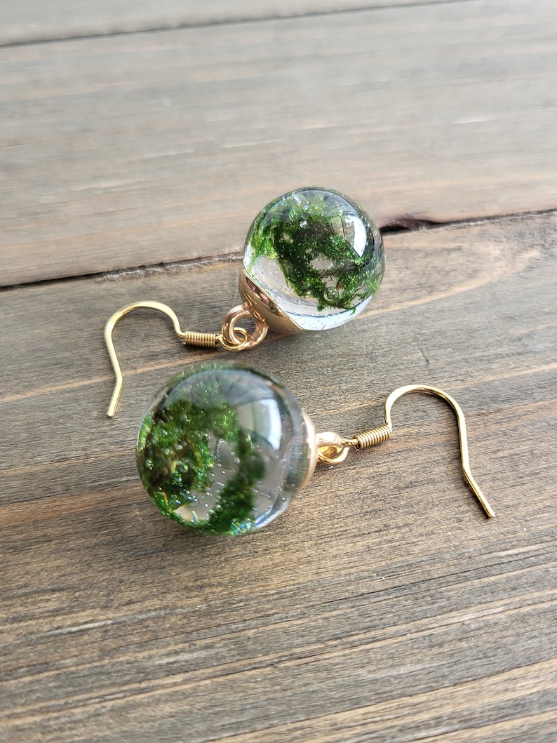 May include: A pair of gold earrings with clear glass spheres containing preserved green moss.