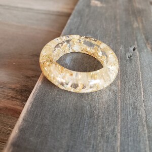 Op de afbeelding: Een transparante harsring met ingebedde gouden vlokken. De ring is dik en heeft een afgeronde vorm.