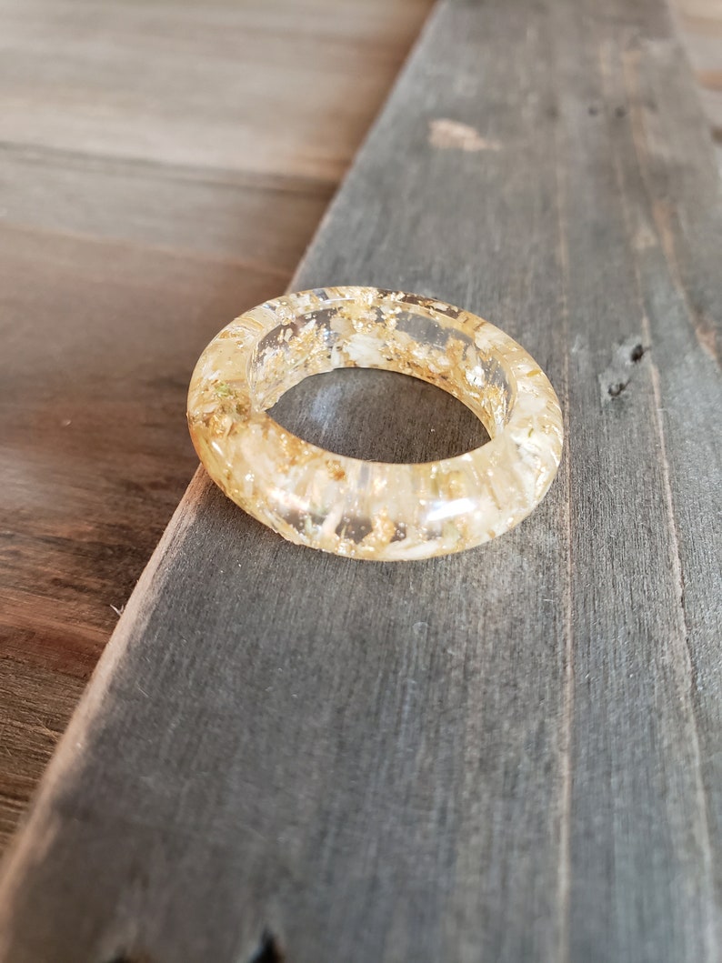 Op de afbeelding: Een transparante harsring met ingebedde gouden vlokken. De ring is dik en heeft een afgeronde vorm.