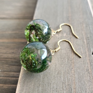 May include: A pair of gold earrings with clear glass orbs containing green moss and glitter.