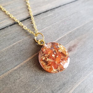 May include: A gold chain necklace with a round pendant featuring a resin design with orange and gold flakes.