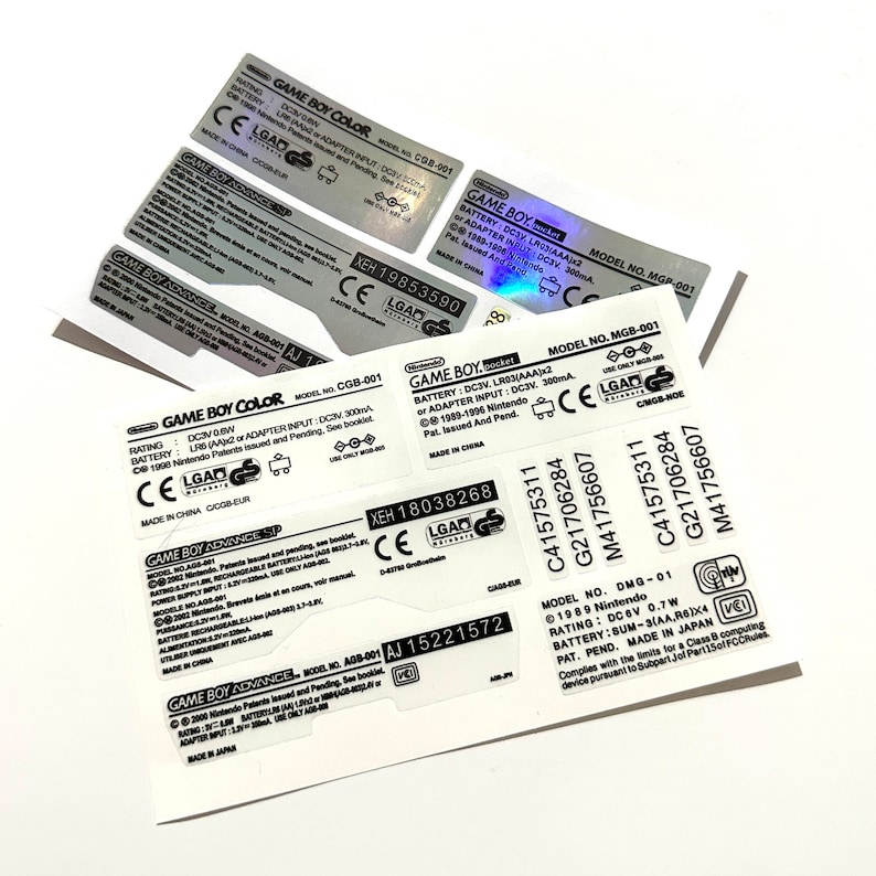 May include: Close-up of a silver and black Game Boy Color sticker with the text "GAME BOY COLOR" and "MODEL NO. CGB-001". The sticker also includes the text "RATING: DC3V 0.8W", "BATTERY: LR6 (AA) or ADAPTER INPUT: DC3V 300mA", "CE", "LGAD", and "MADE IN CHINA CGB-EUR".