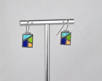 May include: Square earrings with a geometric design. Each earring features a silver frame with a mosaic of colorful shapes in blue, green, orange, and turquoise. The earrings hang from silver hooks.