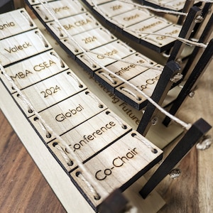May include: A wooden model of a bridge with small wooden signs hanging from it. The signs have text on them, including "MBA CSEA 2024", "Global", "Conference", and "Co-Chair".
