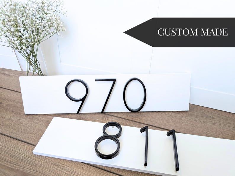 White Horizontal 18 in x 5.5 in x 1/2 in thick rectangular address plaques with modern black metal numbers. One plaque displays the numbers 970, and the other shows 811. The words "CUSTOM MADE" are in a black arrow shape in the background.