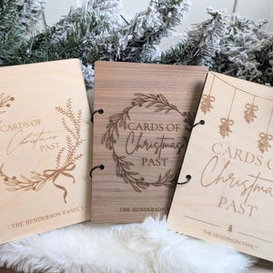 May include: Three wooden Christmas card holders with the text "CARDS OF Christmas PAST" and "THE HENDERSON FAMILY" engraved on them. The holders have different designs, including wreaths and hanging ornaments.