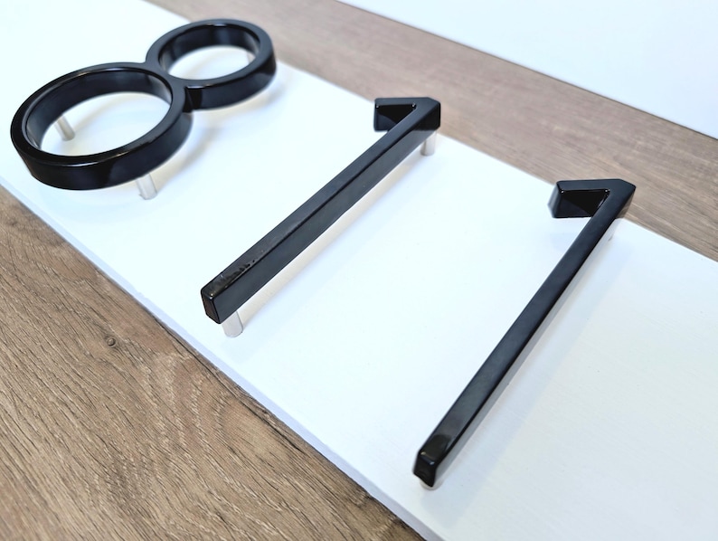 A close up side view of a Horizontal modern house number sign featuring the modern black metal numbers "811", shown floating mounted (intentionlly lifted to create space between numbers and plaque) onto a wooden white rectangular 18 in x 5.5 in x 1/2 in thick plaque.