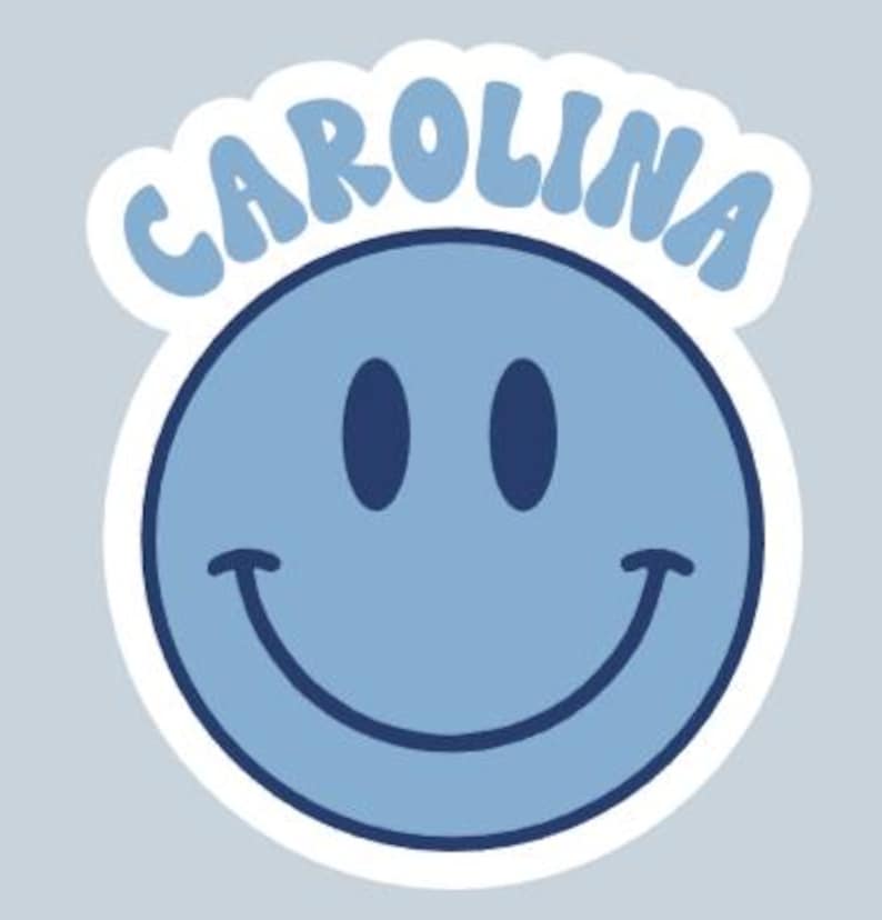 Peut inclure: Un autocollant de visage souriant bleu clair avec le mot "CAROLINA" dans une police bleu clair assortie au-dessus du visage. L'autocollant a une bordure blanche et est pos&eacute; sur un fond gris clair.