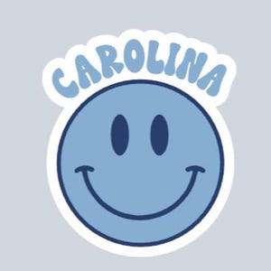 Peut inclure: Autocollant bleu clair avec un smiley et le mot "CAROLINA" en arc au-dessus. Le smiley a des yeux bleu fonc&eacute; et une bouche incurv&eacute;e. L'autocollant a une bordure blanche sur fond gris clair.