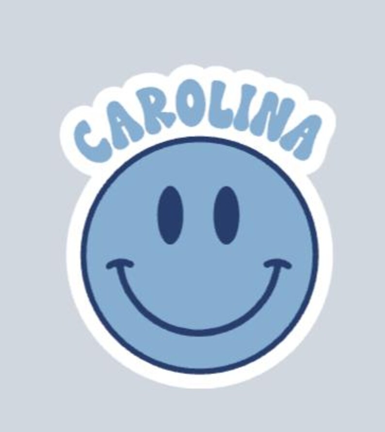 Peut inclure: Autocollant bleu clair avec un smiley et le mot "CAROLINA" en arc au-dessus. Le smiley a des yeux bleu fonc&eacute; et une bouche incurv&eacute;e. L'autocollant a une bordure blanche sur fond gris clair.