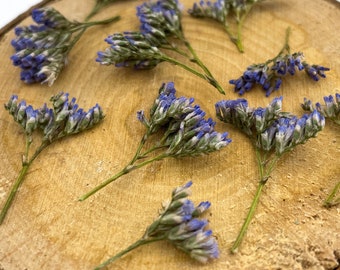 May include: A wooden slice with a natural bark edge, decorated with dried purple flowers. The flowers are arranged in a scattered pattern across the surface of the wood.
