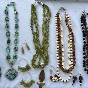 May include: Five necklaces with matching earrings and a bracelet. The necklaces are made of different materials, including green stones, brown and white beads, and black and gray stones. The earrings and bracelet are made of the same materials as the necklaces.