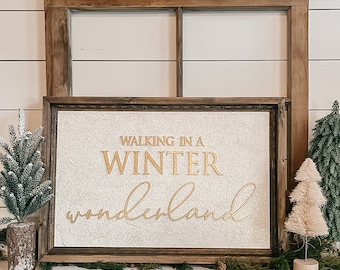 May include: A wooden framed sign with the gold text "WALKING IN A WINTER WONDERLAND". The sign has a textured, off-white background. The scene is decorated with small Christmas trees and a garland of dried orange slices and white pom-poms, creating a winter theme.