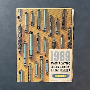 Pu&ograve; includere: Un catalogo vintage Monroe Master del 1969 per ammortizzatori e stabilizzatori di livello di carico. La copertina del catalogo presenta una variet&agrave; di ammortizzatori di diverse dimensioni e stili.