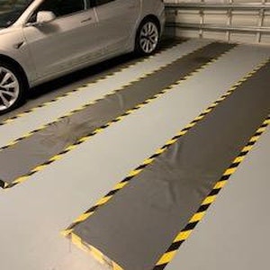 May include: Two gray garage floor mats with black and yellow caution tape markings. The mats are in a garage with a silver Tesla car parked in the background.