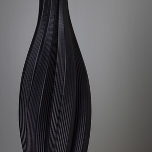 Op de afbeelding: Een zwarte vaas met een getextureerd, geribbeld ontwerp. De vaas heeft een slanke hals en een bredere basis, met verticale lijnen die een vloeiende, elegante vorm cre&euml;ren. De donkere kleur en unieke textuur geven het een moderne, artistieke uitstraling.