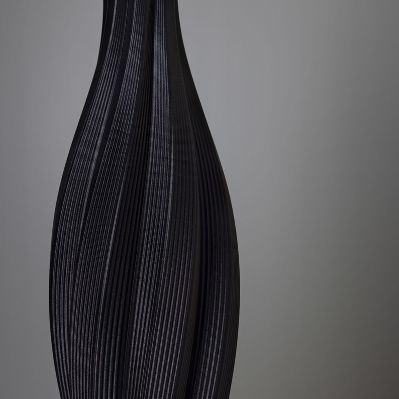 Op de afbeelding: Een zwarte vaas met een getextureerd, geribbeld ontwerp. De vaas heeft een slanke hals en een bredere basis, met verticale lijnen die een vloeiende, elegante vorm cre&euml;ren. De donkere kleur en unieke textuur geven het een moderne, artistieke uitstraling.