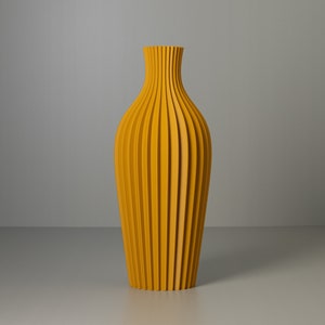 Könnte beinhalten: Eine hohe, gelbe Keramikvase mit geripptem Design. Die Vase ist oben und unten schmal und in der Mitte breiter.