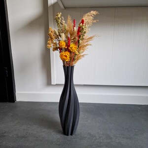 Tall 3D printed black floor vase with twisted shape and stripe texture, showcasing a bouquet of yellow and red dried flowers and pampas grass