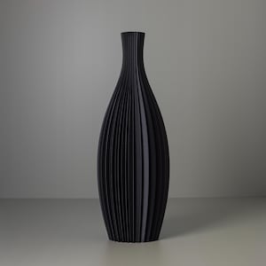 Può includere: Un vaso in ceramica nero con un design plissettato. Il vaso è alto e stretto, con una base arrotondata e un'apertura svasata.
