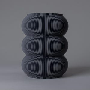 Op de afbeelding: Een donkergrijze, gestapelde vaas met een geribbelde textuur. De vaas bestaat uit drie afgeronde secties, wat een uniek, modern ontwerp creëert. Het bovenste gedeelte heeft een iets bredere opening.