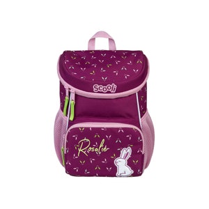 Könnte beinhalten: Ein lila und rosa Rucksack mit einem weißen Hasen und dem Text "Rosalie" auf der Vorderseite. Der Rucksack hat einen grünen Reißverschluss und eine Netztasche an der Seite. Der Rucksack hat ein kleines weißes Etikett mit dem Text "Scooli" darauf.