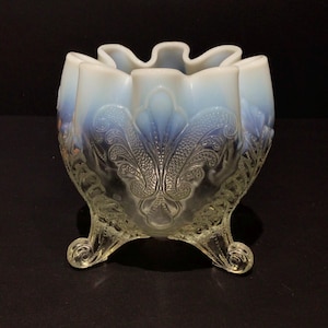 以下が含まれることがあります： 波状の縁と3つの巻き足が付いた、透明でオパールセントなガラスボウル。 ボウルはエンボス加工された花の模様と、微妙な青色の色合いが特徴で、ヴィンテージな美しさを醸し出しています。 ボウルの直径は約15cmです。