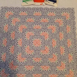 May include: A close-up of a cross-stitch project featuring a geometric pattern of black, green, and red squares. The project is framed and the text "Stitched by Sue" is visible at the bottom.