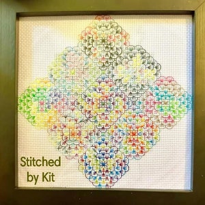 May include: A framed cross-stitch design featuring a colorful geometric pattern of overlapping circles. The text "Stitched by Kit" is in the lower left corner of the image.