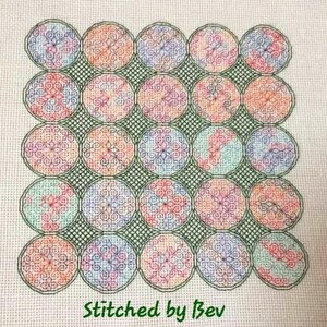 May include: A cross-stitch design featuring a grid of 25 colorful circles with intricate patterns. The circles are outlined in green and arranged in a square shape. The text "Stitched by Bev" is at the bottom of the design.