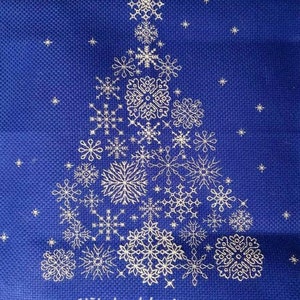 May include: A blue fabric background with a white embroidered Christmas tree design. The tree is made up of many different snowflake designs. The text "Stitched by Laura" is at the bottom of the image.