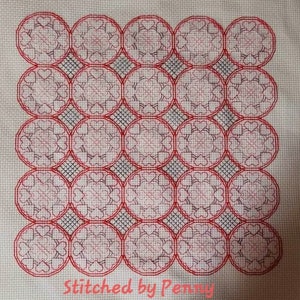 May include: A white fabric with a red and black cross-stitch pattern of repeating circles with hearts inside. The fabric is labeled "Stitched by Penny".