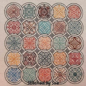May include: A cross-stitch pattern with a repeating design of interlocking circles and squares. The circles and squares are filled with different colored floral patterns. The background is a light beige color. "Stitched by Sue" is written in the bottom right corner.