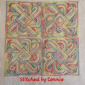 May include: A cross-stitch design with four squares featuring a repeating pattern of interlocking loops in red, blue, green, and yellow. The design is stitched on a white canvas and includes the text "Stitched by Connie".