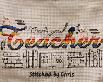 Op de afbeelding: Borduurwerk met kruissteek van het woord "Teacher" in regenboogkleuren met een rode appel en potloden. Het woord "Thank you" is geborduurd boven het woord "Teacher". Onder het woord "Teacher" staan stapels boeken, een alfabetblok en een cijferblok. De tekst "Stitched by Chris" is geborduurd onder de boeken.