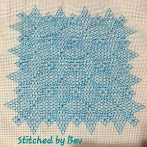 May include: A blue and white cross-stitch pattern with a geometric design. The pattern is stitched on a white fabric and features a repeating pattern of stars and diamonds. The text "Stitched by Bev" is at the bottom of the image.