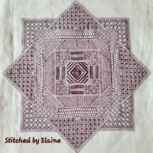 Può includere: Un primo piano di un disegno a punto croce marrone e bianco su uno sfondo di tessuto bianco. Il disegno è un motivo geometrico con una forma a stella al centro. Il testo "Stitched by Elaine" è in basso nell'immagine.